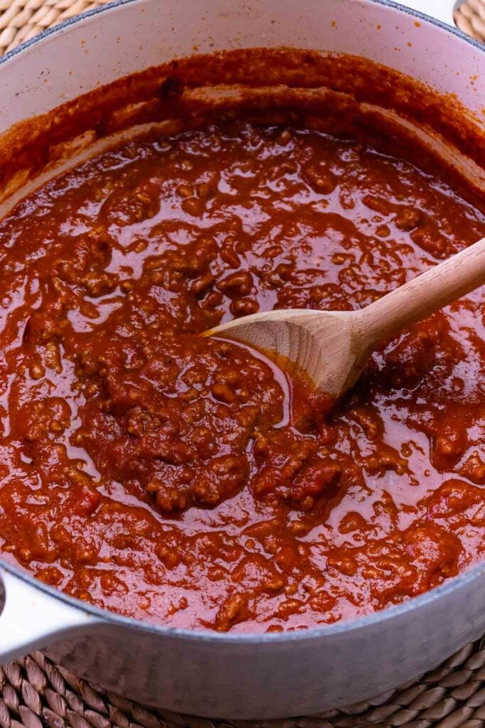 Homemade spaghetti sauce with ground beef in a white cast iron pot with a wooden spoon.