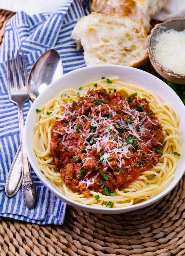 Bowl of homemade spaghetti sauce over noodles with a spoonn and fork for serving.