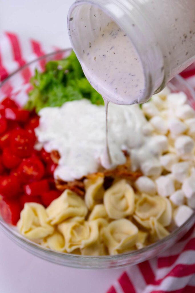 Ranch dressing poured over ingredients for BLT Tortellini Pasta Salad.