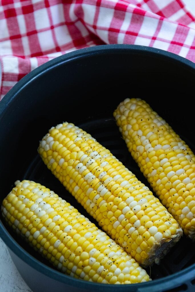 Corn on the cob with salt and pepper in the basket of an air fryer.