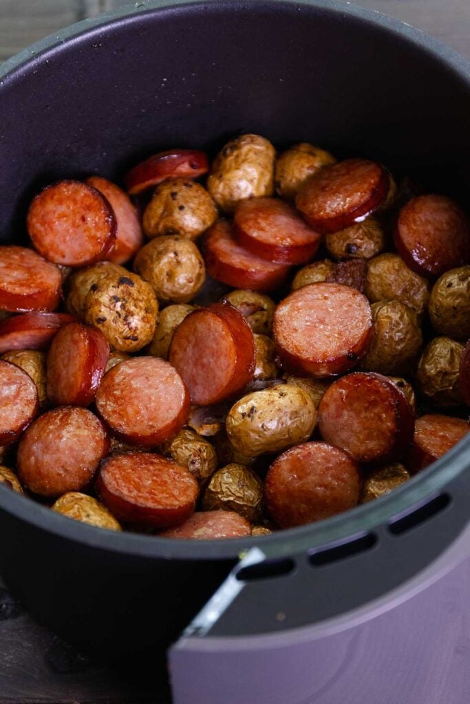 Basket of Air Fryer filled with baby potatoes and smoked kielbasa.