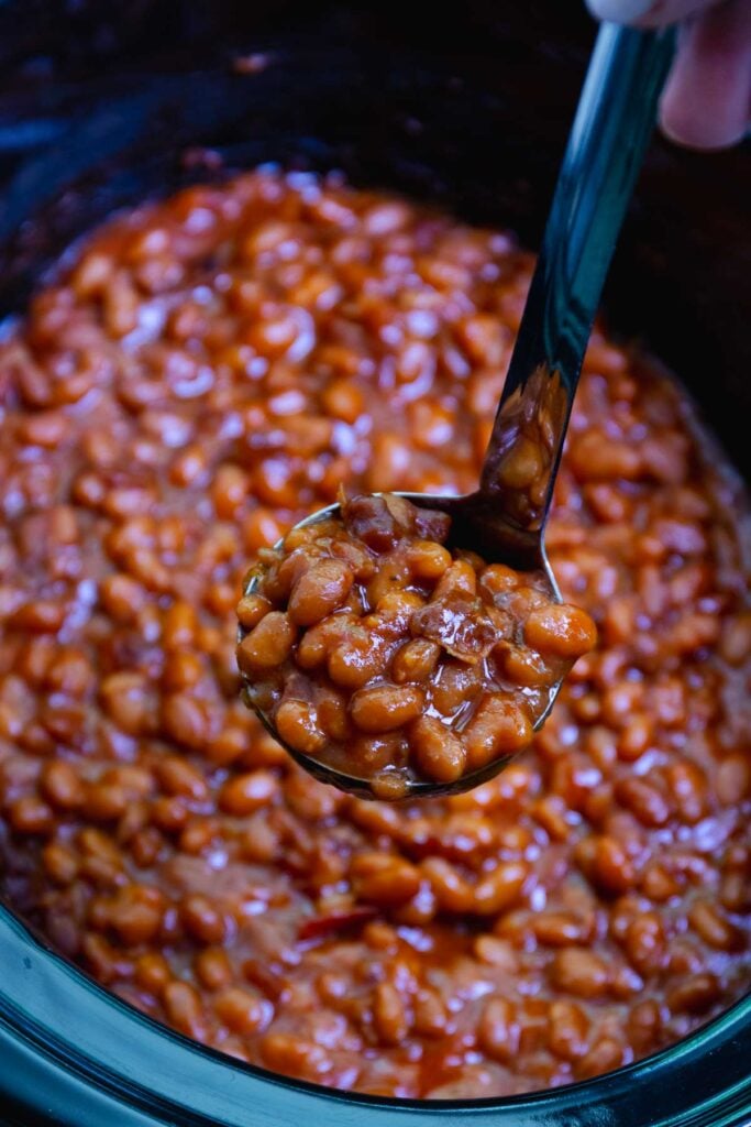 Ladle full of Crock Pot Baked Beans to serve at any summer gathering.
