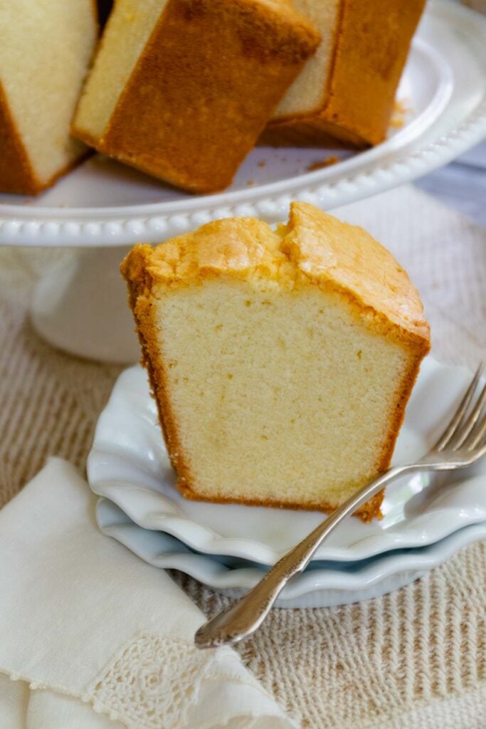 Slice of Million Dollar Pound Cake on a white plate along with sliced of cake served for dessert.
