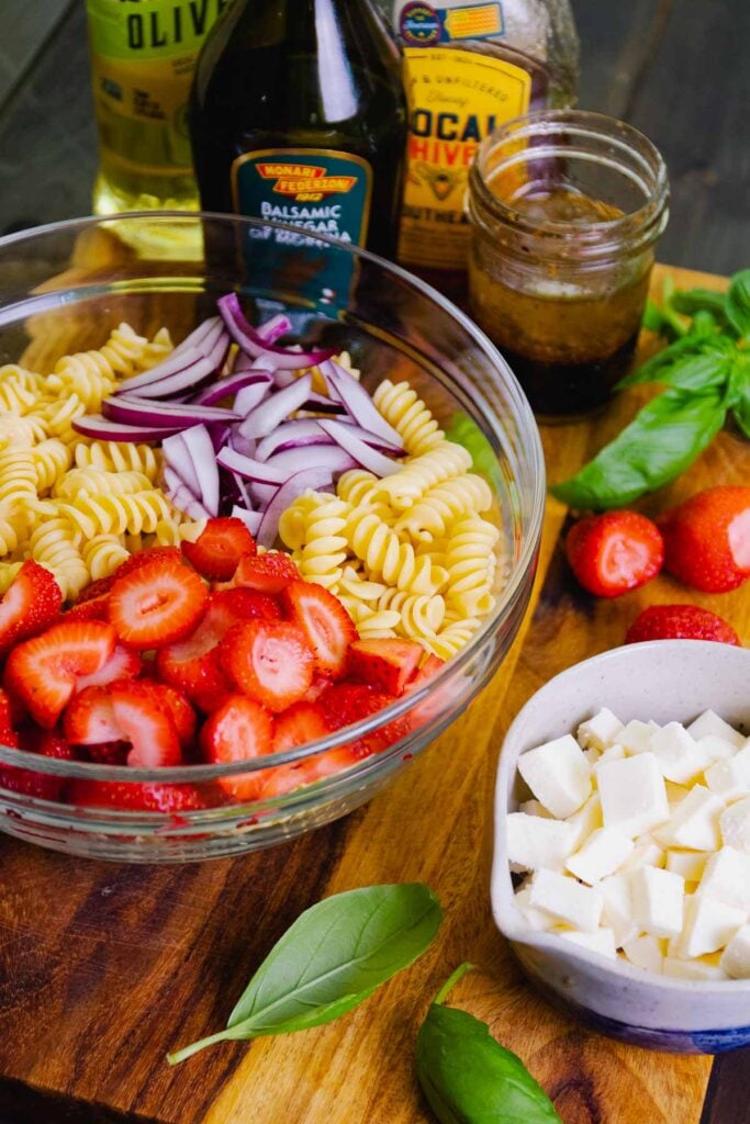 Strawberries, pasta, red onions, mozzarells, fresh basil and dressing for a caprese salad.