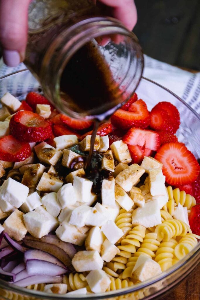 Homemade balsamic dressing poured of ingredients for Strawberry Caprese Pasta Salad.