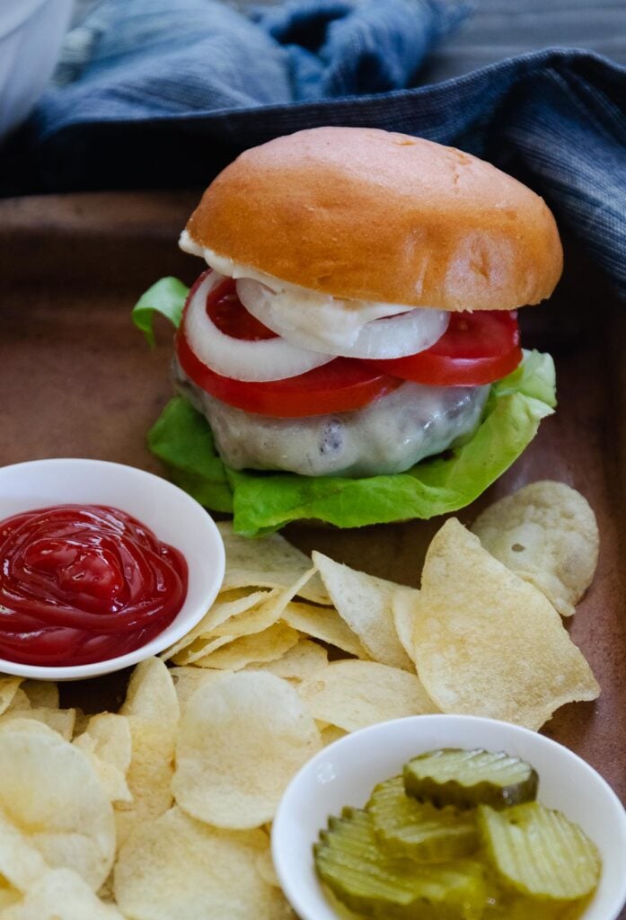 A perfectly cooked cheeseburger served with chips and pickles.