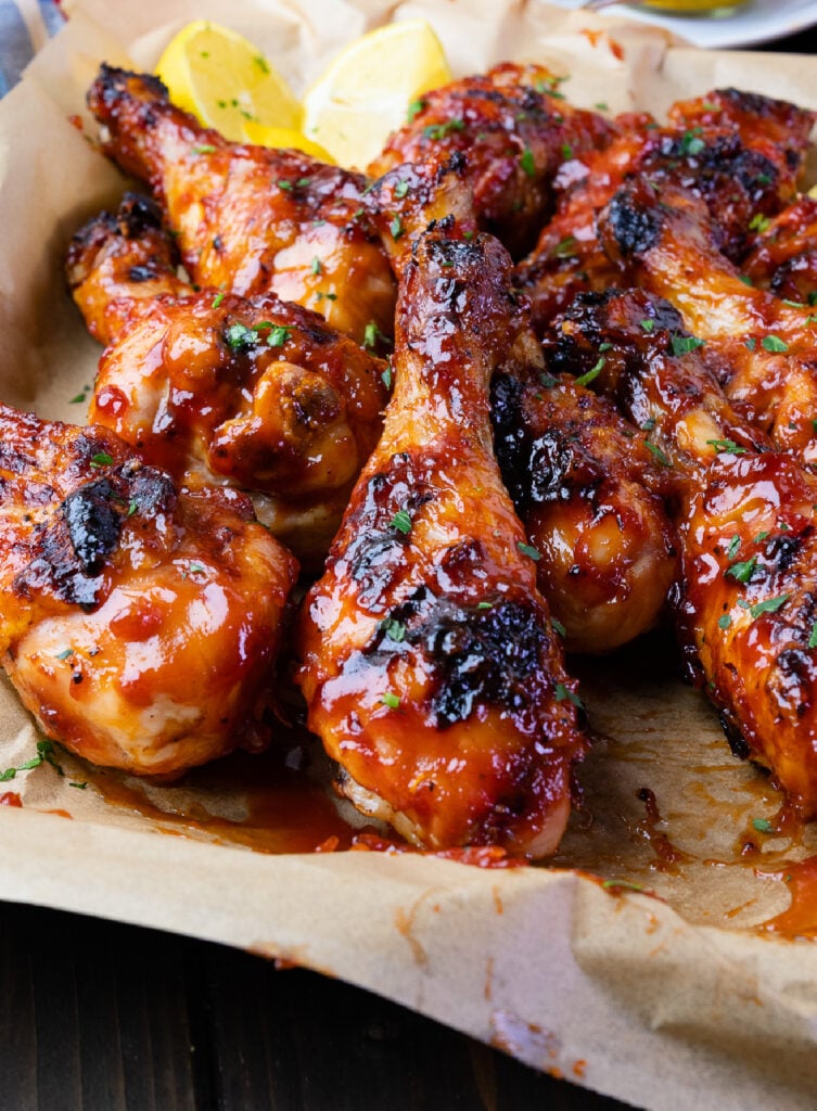 Glazed chicken drumsticks with homemade BBQ sauce on parchment paper, garnished with green onions and lemon wedges