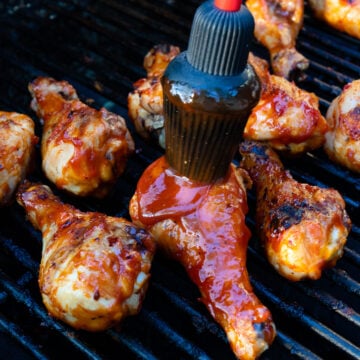 Glazing chicken pieces on grill grates with Homemade BBQ Sauce (Easy And Delicious) using a red-handled brush, charred and caramelized