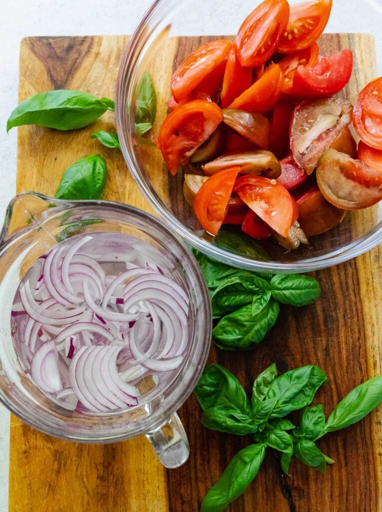 Fresh tomatoes, basil, and red onion soaking in water prepped for making a summer Tomato Salad.