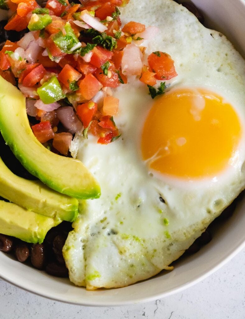 Fried egg for breakfast burrito bowls served with salsa and avocado.