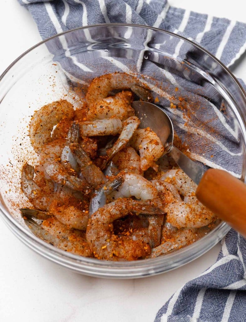 Raw shrimp sprinkled with garlic and Cajun seasoning ready to be cooked in a non-stick skillet.