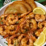 Beautiful white bowl filled with cooked cajun garlic shrimp served with toast and lemons then garnished with fresh parsley as an appetizer or main dish.
