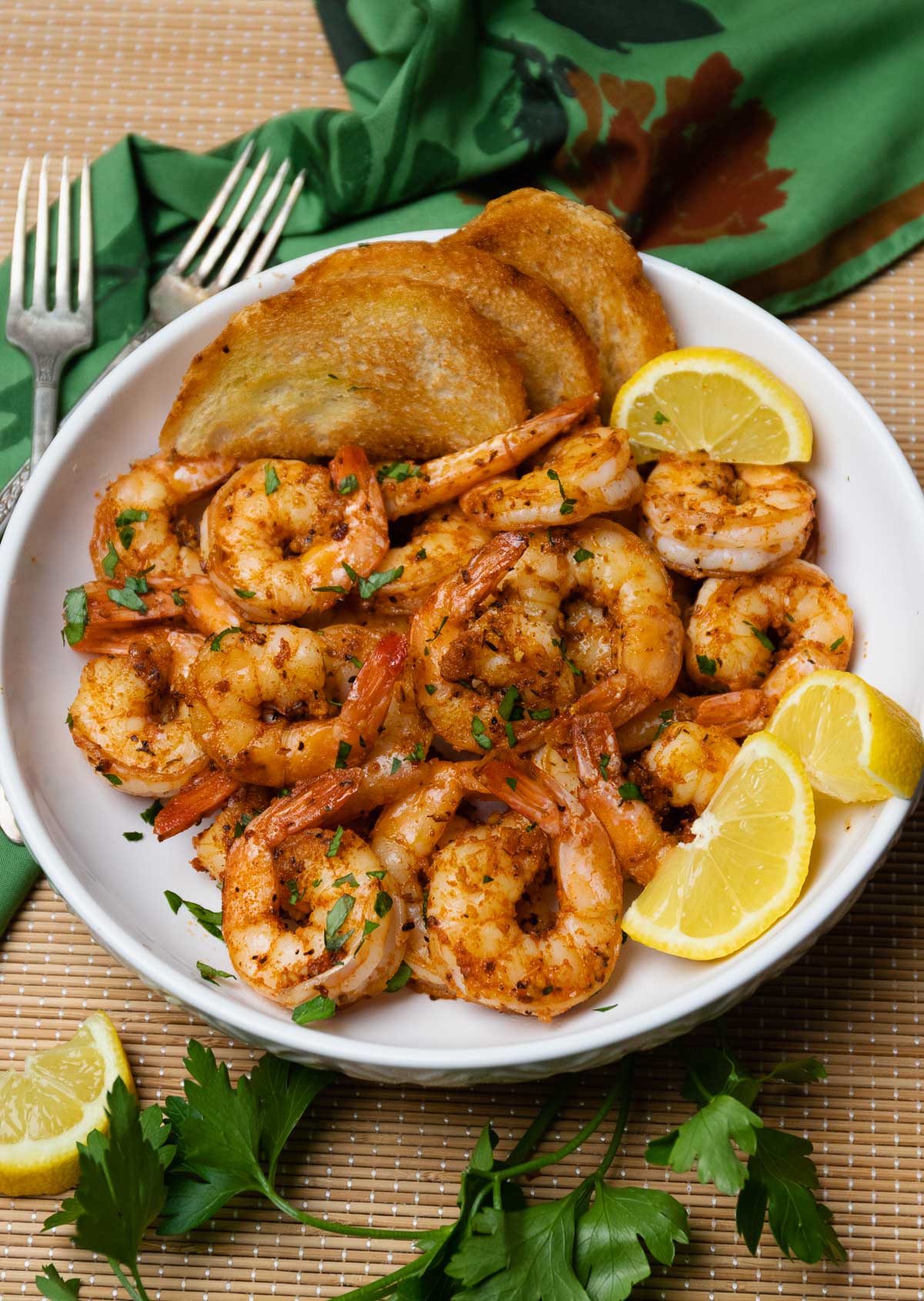 Beautiful white bowl filled with cooked cajun garlic shrimp served with toast and lemons then garnished with fresh parsley.