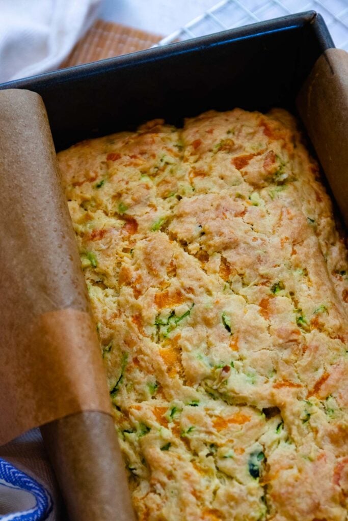 Beautifully baked zucchini cheese bread in a loaf pan lined with parchment.