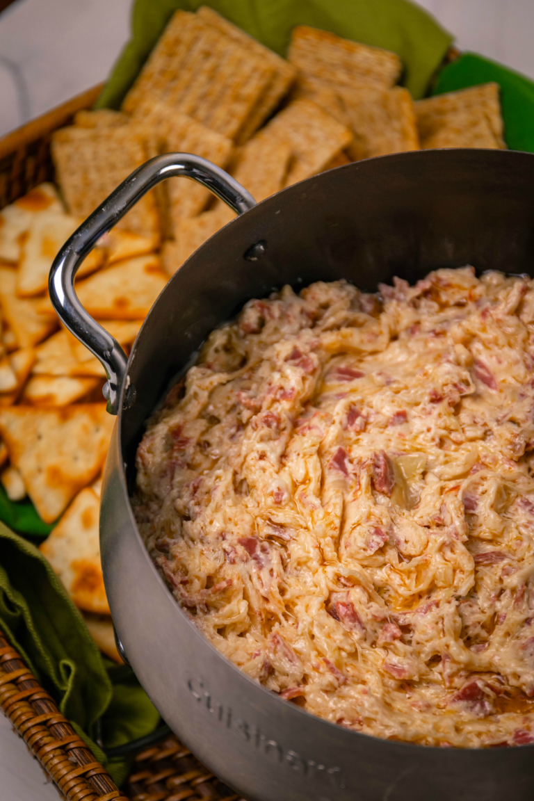 Slow cooker filled with creamy pimento cheese dip studded with ham pieces, surrounded by cheese crackers on a woven placemat for Easy Slow C