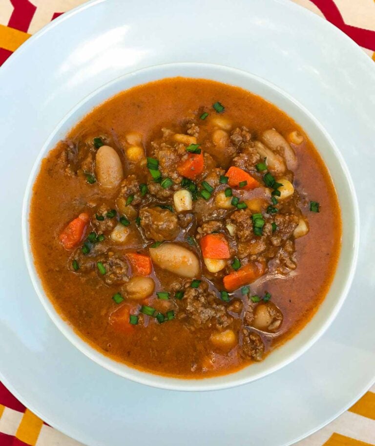 Overhead view of beef and bean chili in white bowl with carrots, beans, and green onion garnish for Easy Slow Cooker Dinners for Busy Weekni