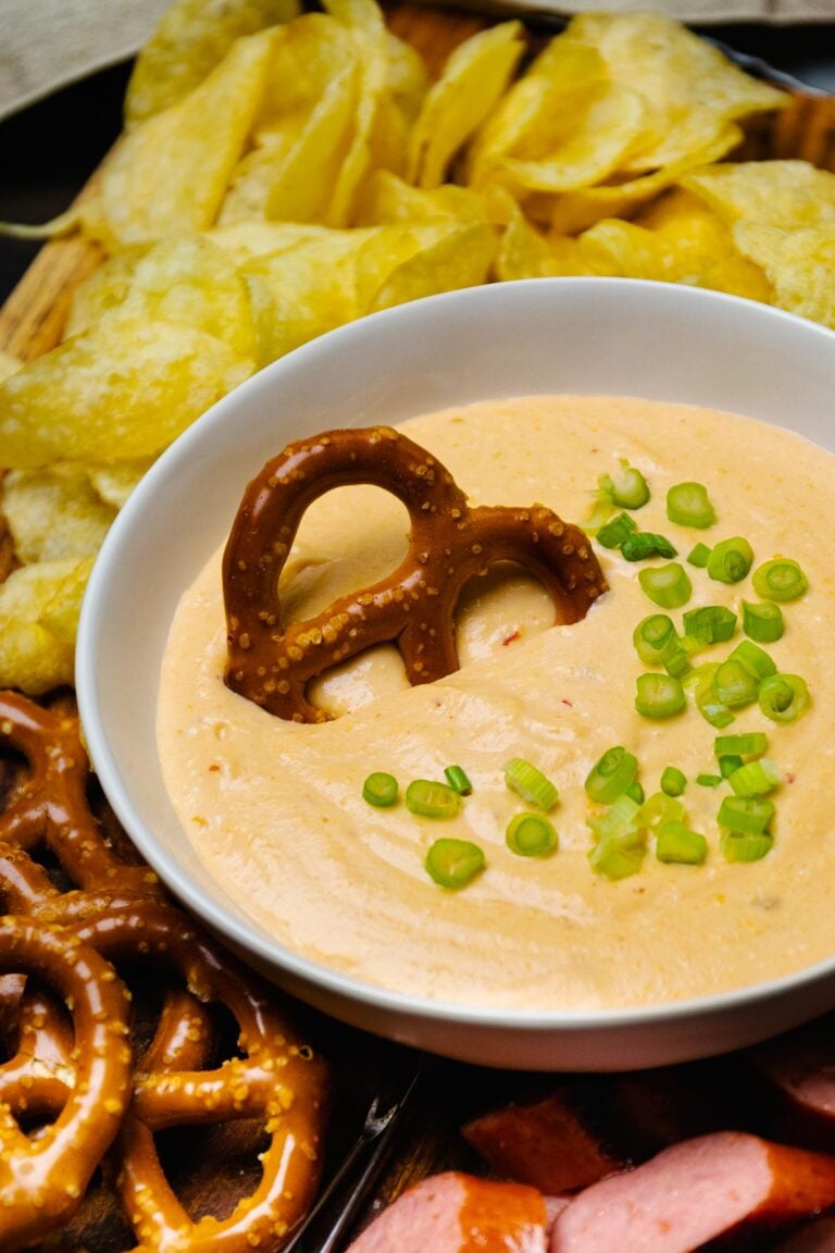 Large white bowl with Beer Cheese Dip topped with green onions served with sausage and pretzels.