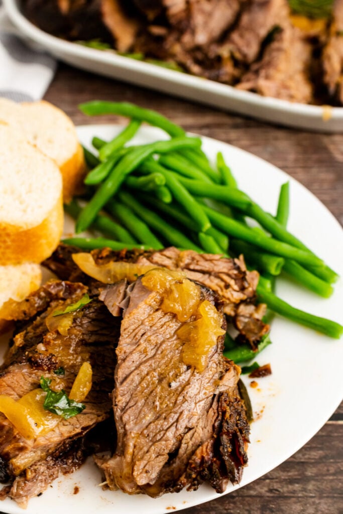 Sliced pot roast with caramelized onions, green beans, and mashed potatoes on white plate for Easy Slow Cooker Dinners for Busy Weeknights
