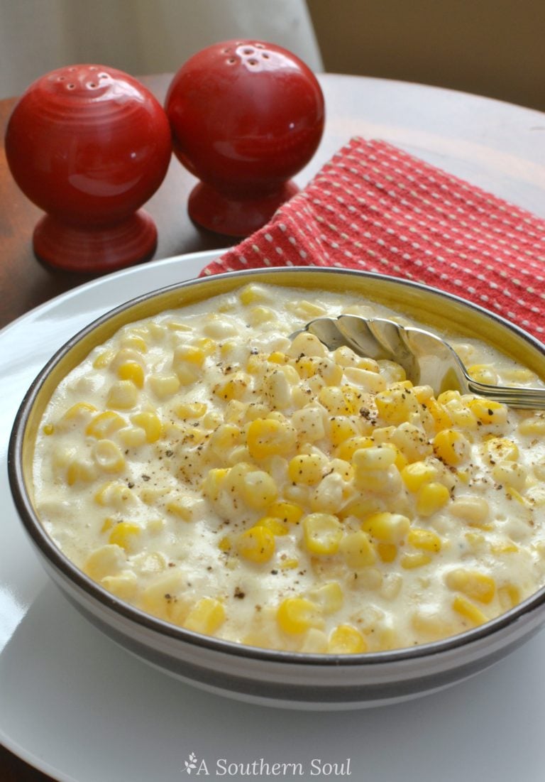 Creamy corn chowder in white bowl with black spoon, topped with black pepper, red salt and pepper shakers, red checkered napkin, Easy Slow C