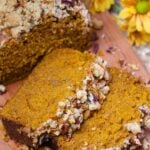 Sliced pumpkin pecan quick bread with crumb topping on wooden board beside yellow flowers