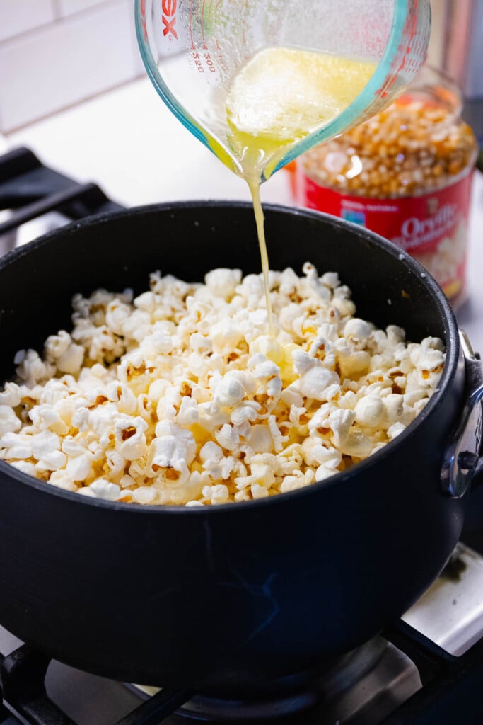 Pouring melted butter over stovetop popcorn.