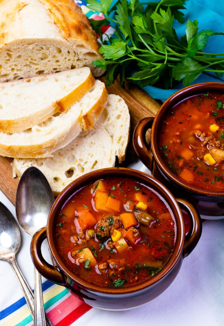 Two bowls of hearty beef and vegetable stew with corn and peppers, served with crusty bread and fresh parsley for Easy Slow Cooker Dinners f