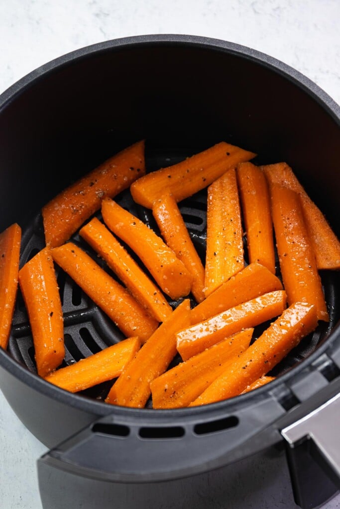 Sliced carrots seasoned with garlic powder, salt and pepper in the basket of an air fryer to be cooked in just 12 minutes.