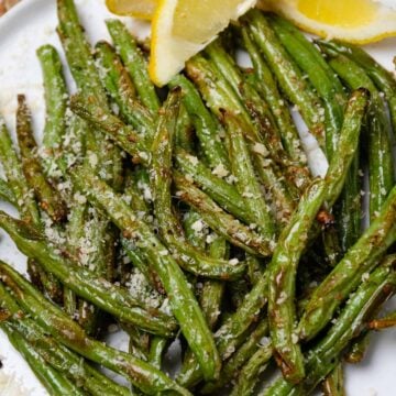 Air Fryer Green Beans (Quick And Easy) plated on white dish, garnished with parmesan and lemon slices