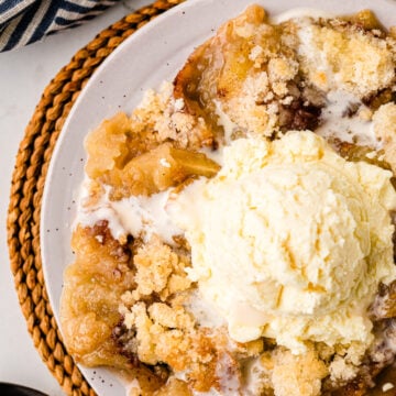 Grandma's Apple Crisp served on a white plate with vanilla ice cream, topped with cinnamon sugar crumble, next to a striped napkin