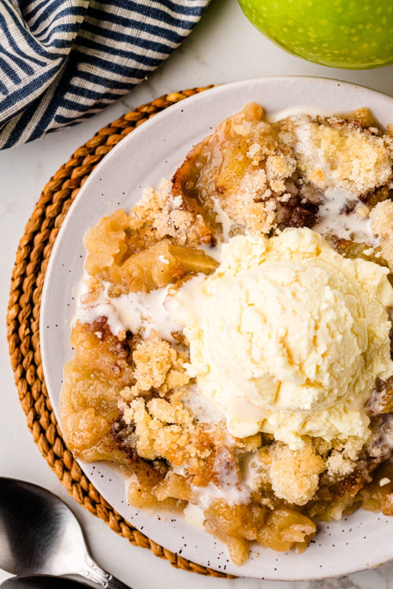 Grandma's Apple Crisp served on a white plate with vanilla ice cream, topped with cinnamon sugar crumble, next to a striped napkin