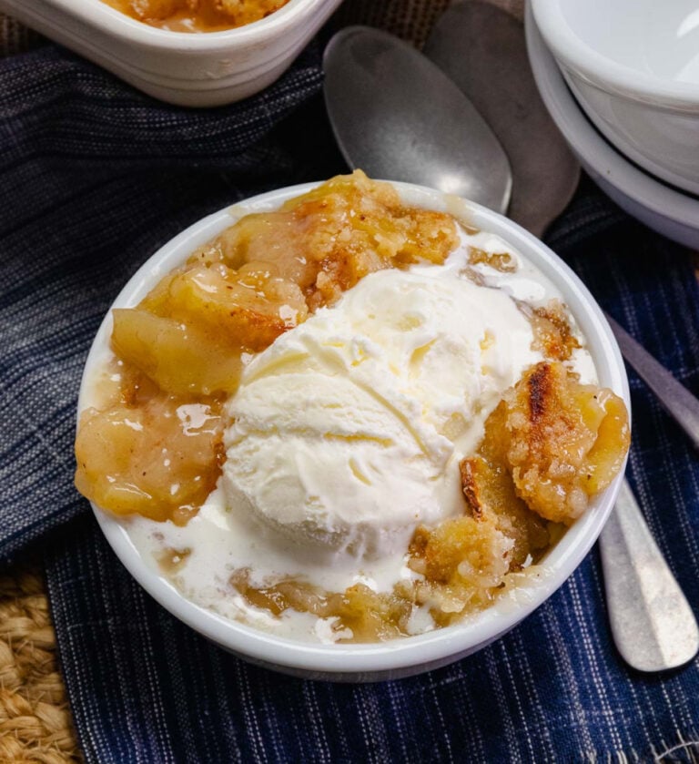 Grandma's Apple Crisp served in a white bowl with vanilla ice cream melting over warm spiced apples and cinnamon crumble topping