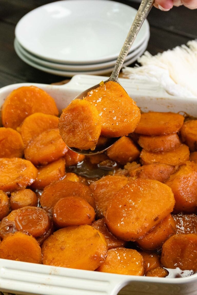 Southern Candied Sweet Potatoes served in a white dish with a spoon lifting a piece, showing the glossy caramelized coating and syrup