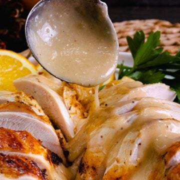 Spoon drizzling creamy turkey gravy over sliced roasted turkey with lemon and parsley garnish, How To Make Turkey Gravy