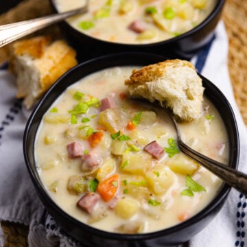 Crock Pot Ham And Potato Soup in black bowls with crusty bread, garnished with green onions and diced ham