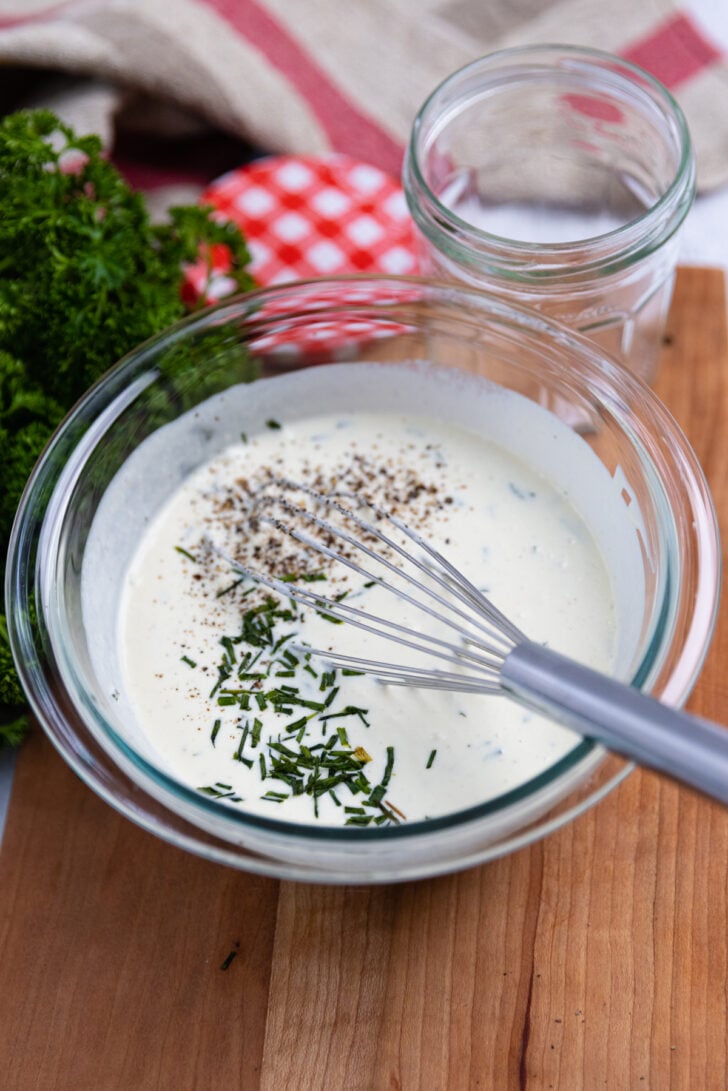 Mixing bowl with creamy vinaigrette seasoned with fresh cracked pepper and chives.