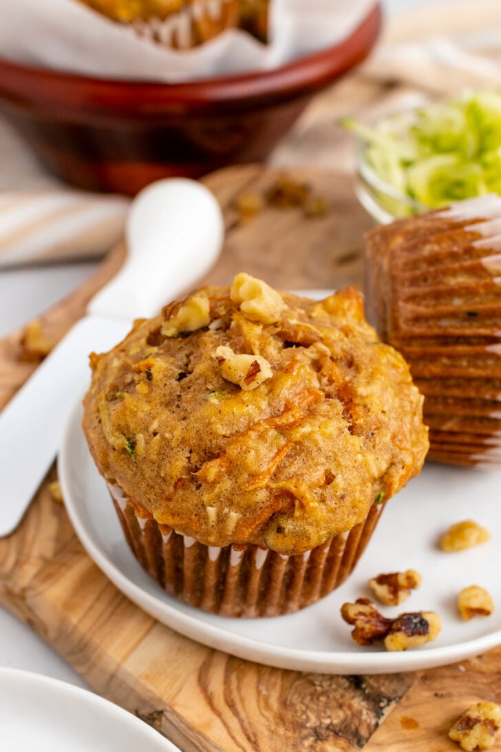 Golden morning glory muffins 6 topped with chopped nuts in brown paper liners on white plate with wooden spoon