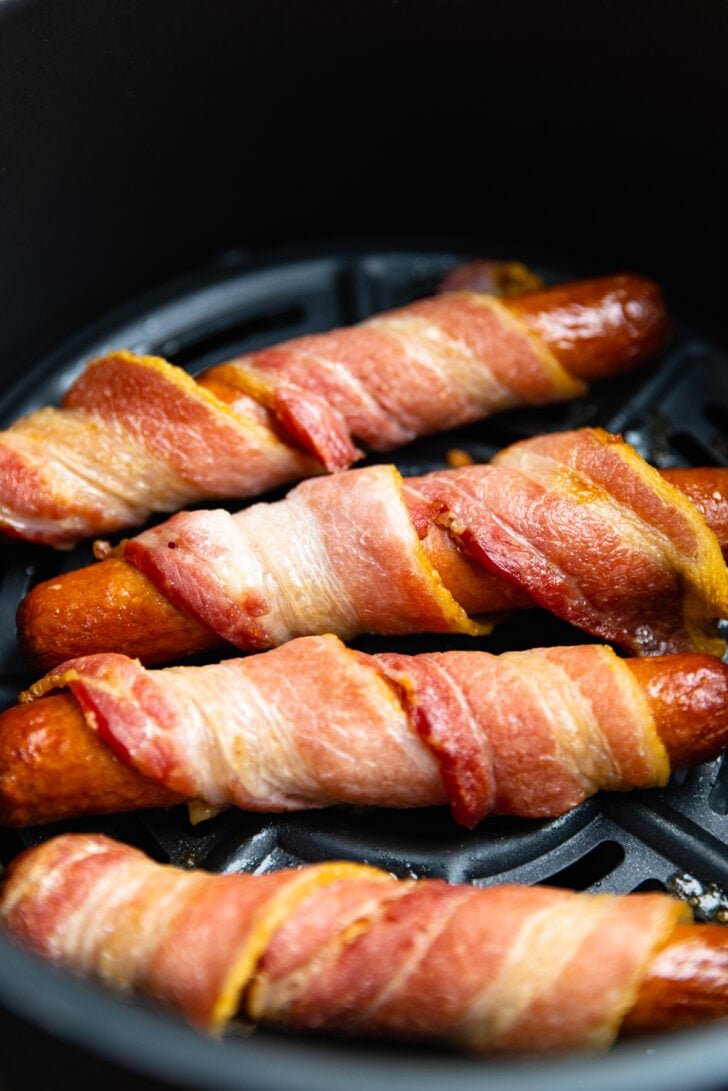 hot dogs wrapped in bacon being cooked in the air fryer