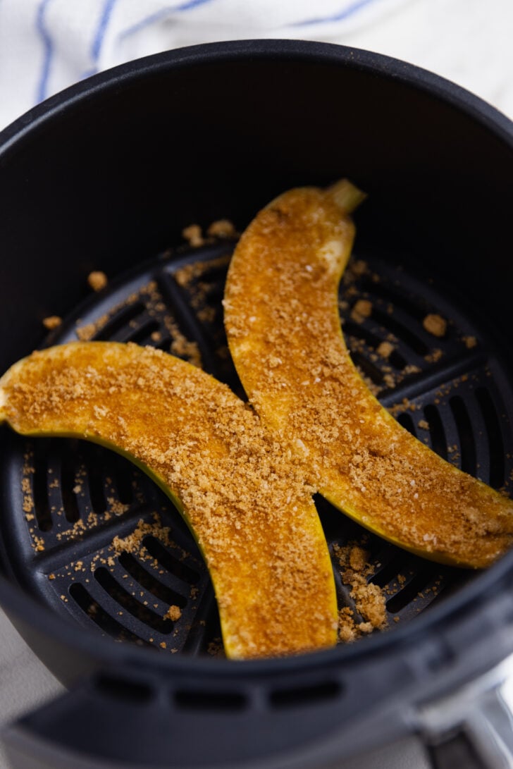 Bananas sliced in half in the basket of an air fryer topped with brown sugar and cinnamon ready to be cooked and served for dessert.