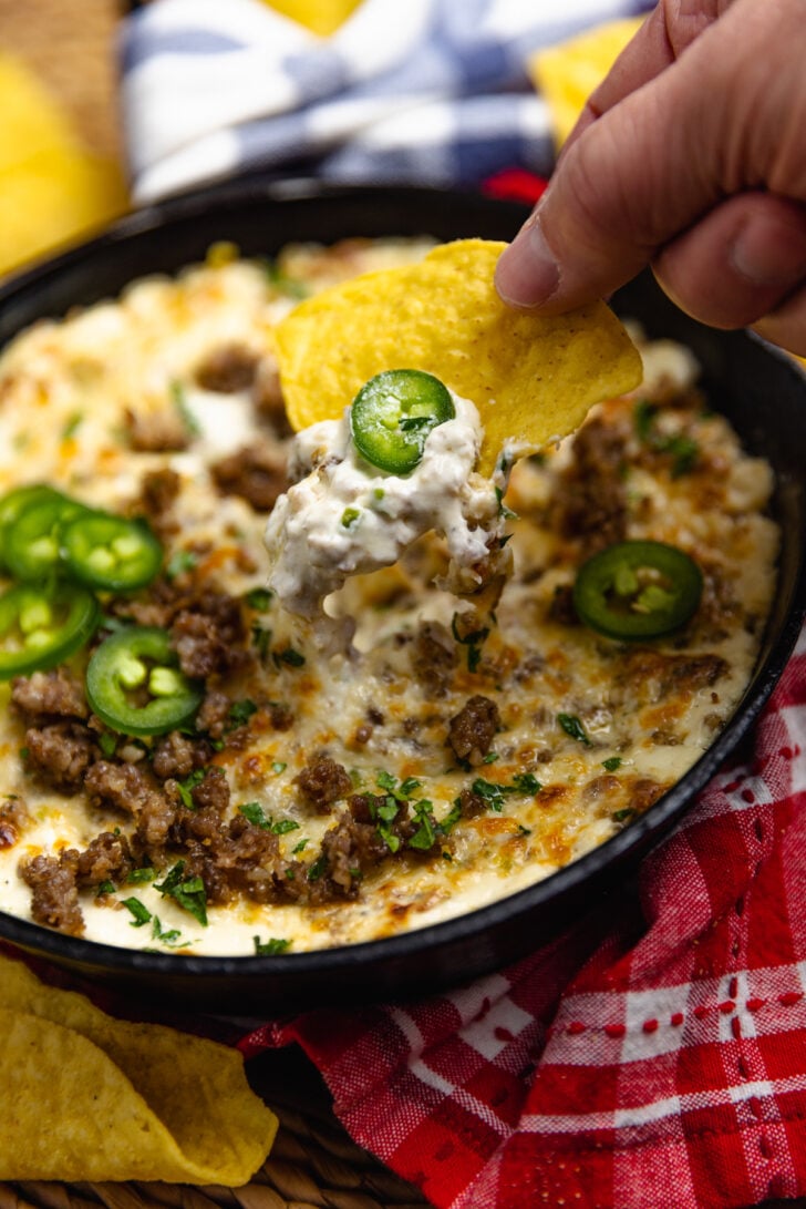 Tortilla chip dipped into Sausage Jalapeno Popper Dip baked in a cast iron skillet is creamy, meaty and spicy. It's a great hot appetizer to serve at family gatherings, parties, game day or anytime you are feeding a crowd.