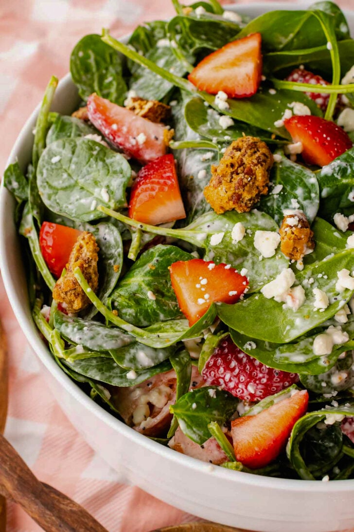 Strawberry Spinach Salad in white bowl with fresh berries, candied nuts, crumbled cheese, and creamy dressing drizzled over greens