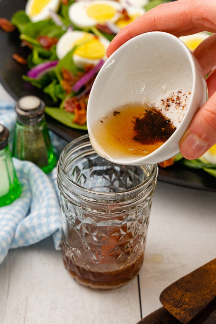 Bacon dripping being added to oil and vinegar, salt, pepper and mustard for homemade warm bacon dressing for spinach salad.