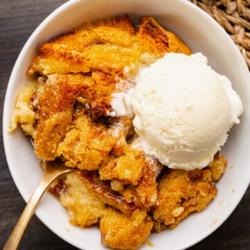 Easy Bread Pudding Recipe served in white bowl with vanilla ice cream scoop and spoon on dark surface