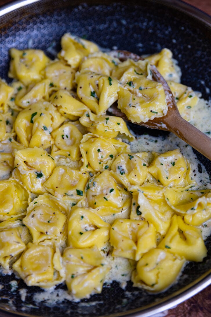 Cheese tortellini cooked in a cream sauce in a skillet on the stove top and serve as a side dish. It's topped with fresh parsley and parmesan cheese.