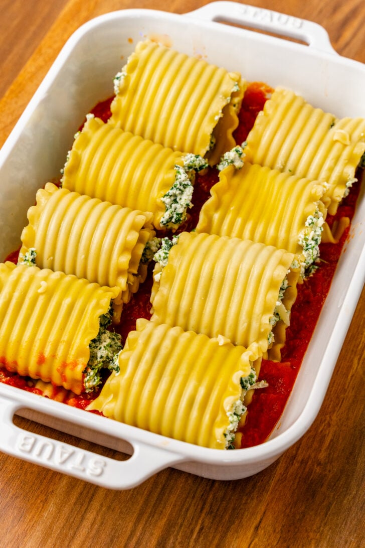 Lasagna noodles stuffed with spinach and cheese with tomato sauce in a casserole dish.