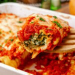 Spinach and cheese lasagna rolls 3 2 1 topped with marinara sauce and melted cheese, garnished with fresh parsley on a white plate