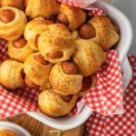 Crescent roll pigs in a blanket in a serving dish and small places served for as an appetizer with toothpicks.