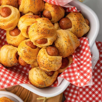 Crescent roll pigs in a blanket in a serving dish and small places served for as an appetizer with toothpicks.
