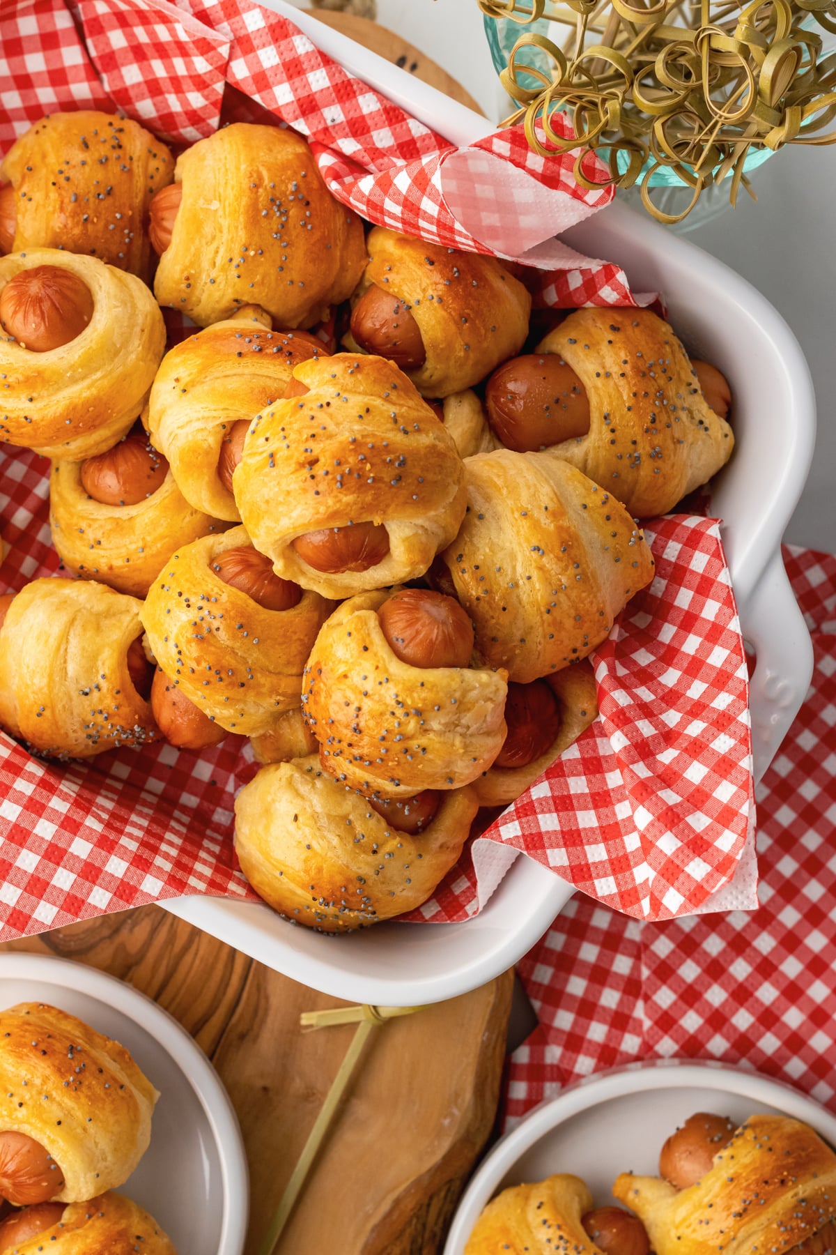Crescent roll pigs in a blanket in a serving dish and small places served for as an appetizer with toothpicks.