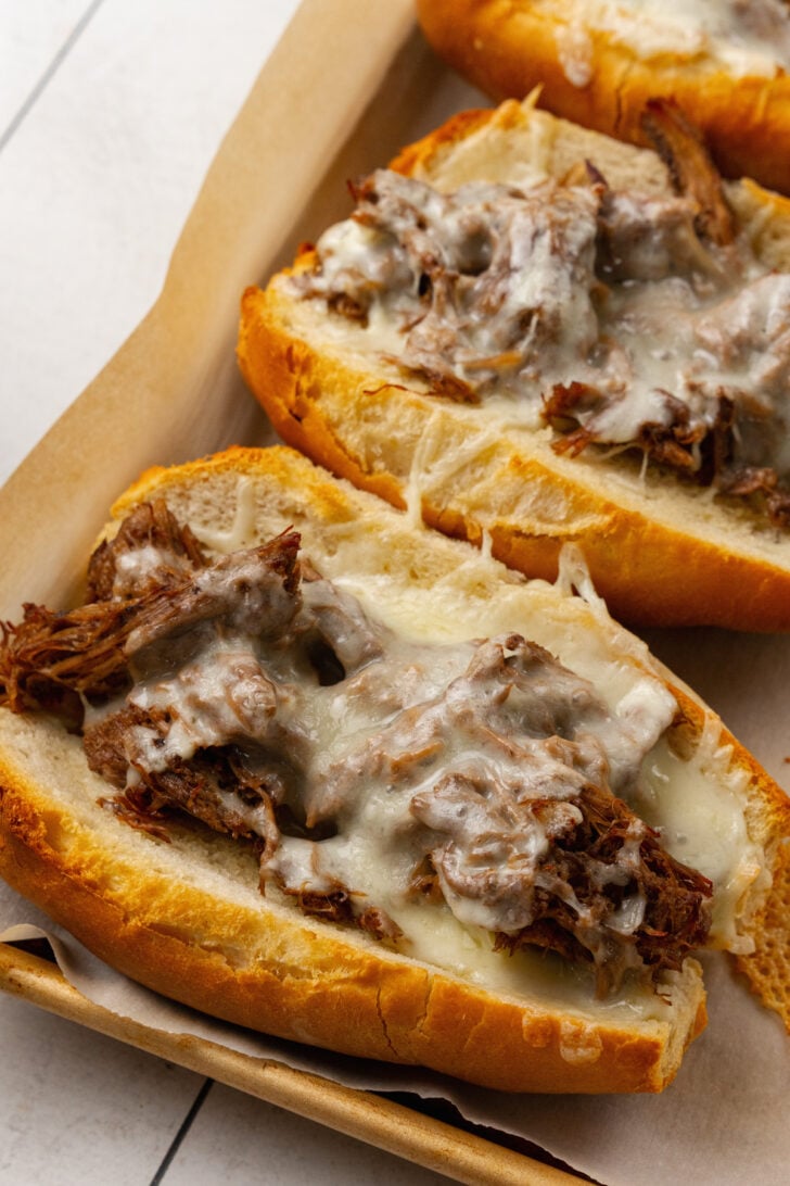 Toasted hoagie buns filled with leftover roast beef, and cheese cooked on parchment paper.