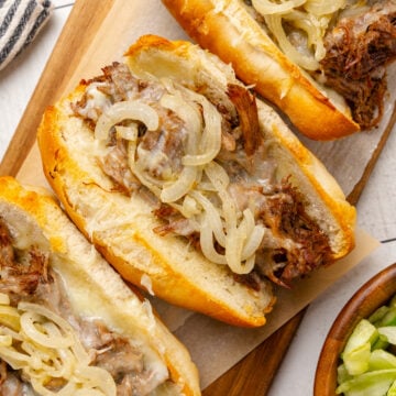 Roast beef sandwiches with melted cheese and sauteed onions in toasted buns are served with a side salad for a delicious weeknight meal, game day, or a get-together with friends.